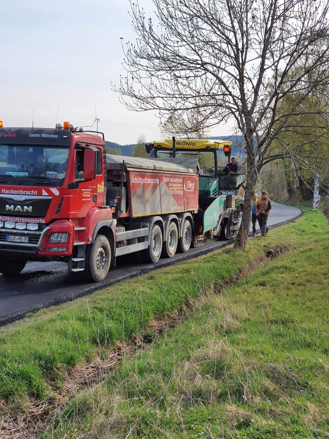 MAN-Kipper mit Schüttguttransporte-Plane beschickt einen Straßenfertiger