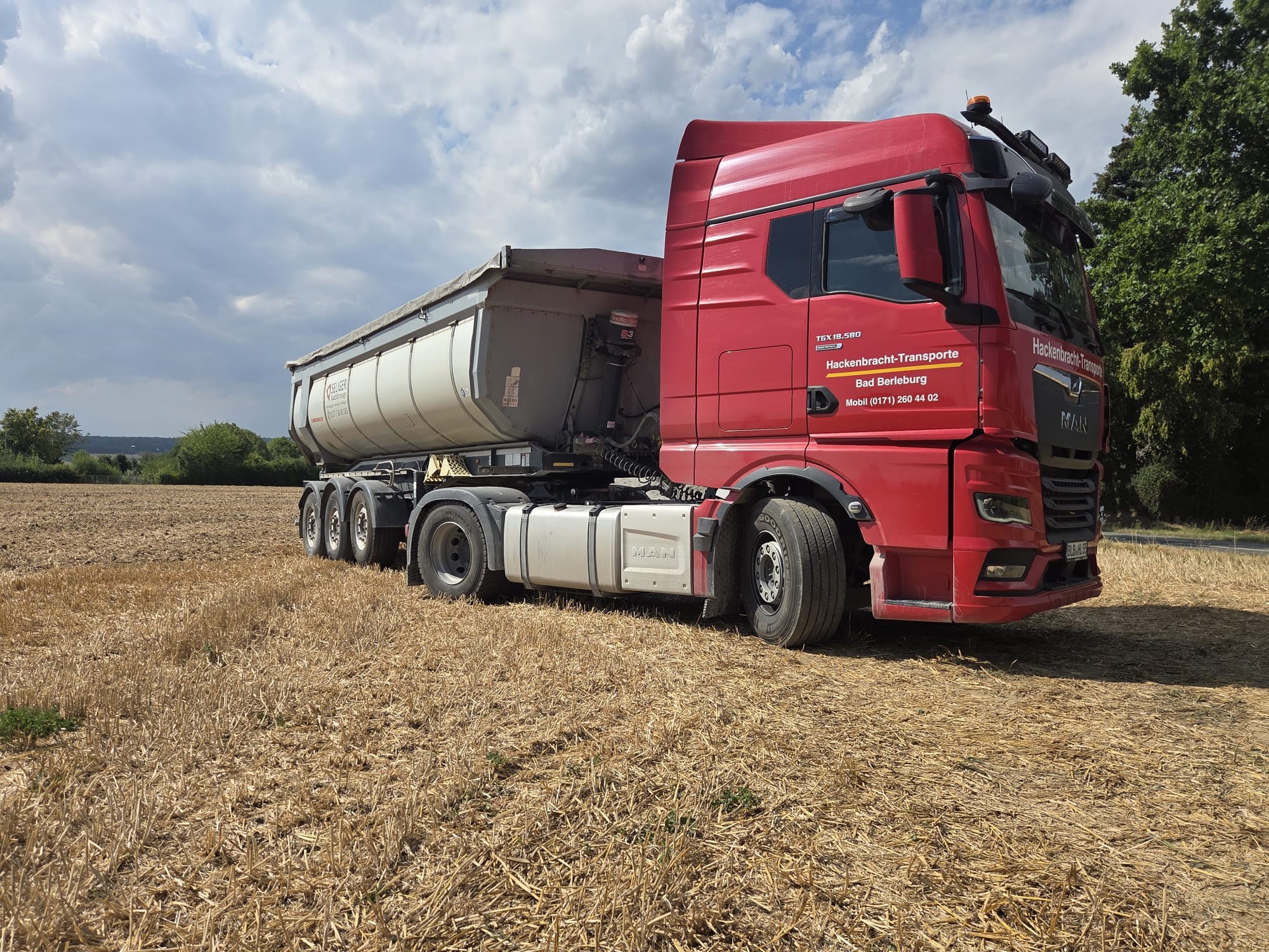 Roter MAN TGX von Hackenbracht-Transporte mit Kippsattelauflieger auf einem Feldweg
